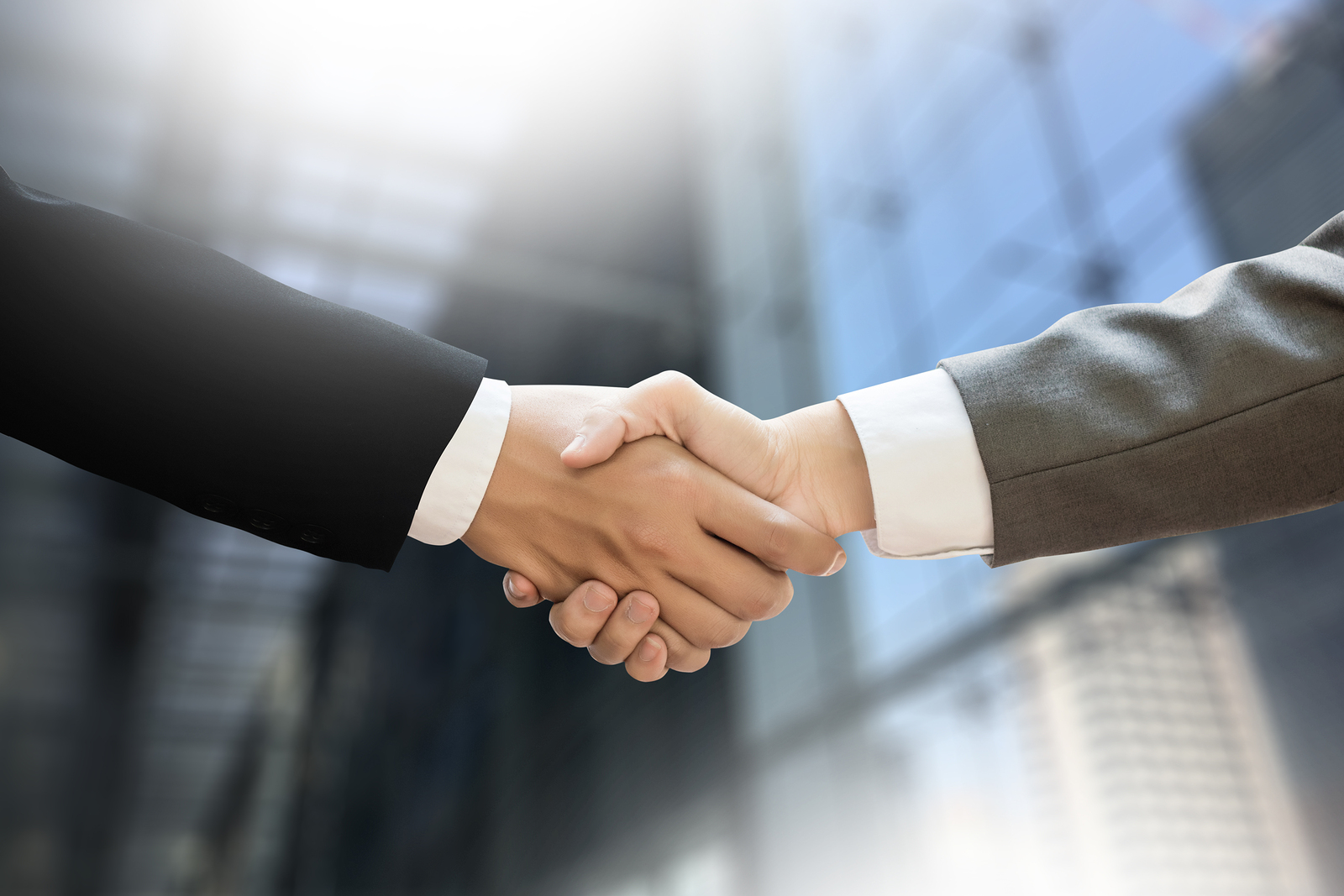 Dwóch biznesmenów w garniturach ściskających dłonie na tle zatłoczonej sali konferencyjnej