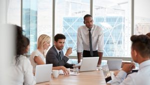 Businessman,Stands,To,Address,Meeting,Around,Board,Table